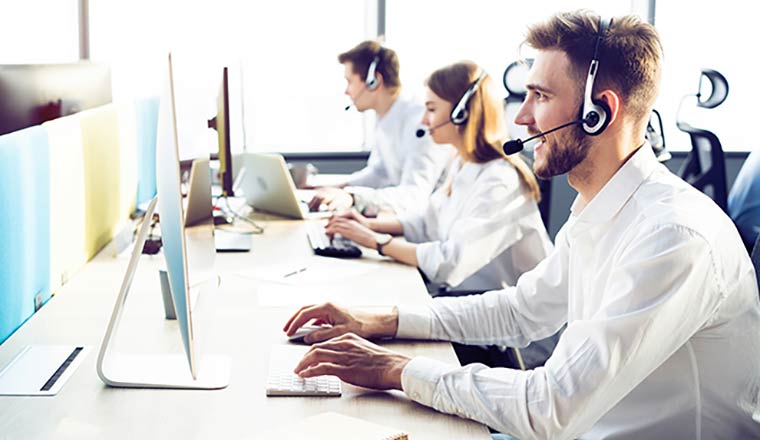 Three happy advisors work at a desk in front of computers