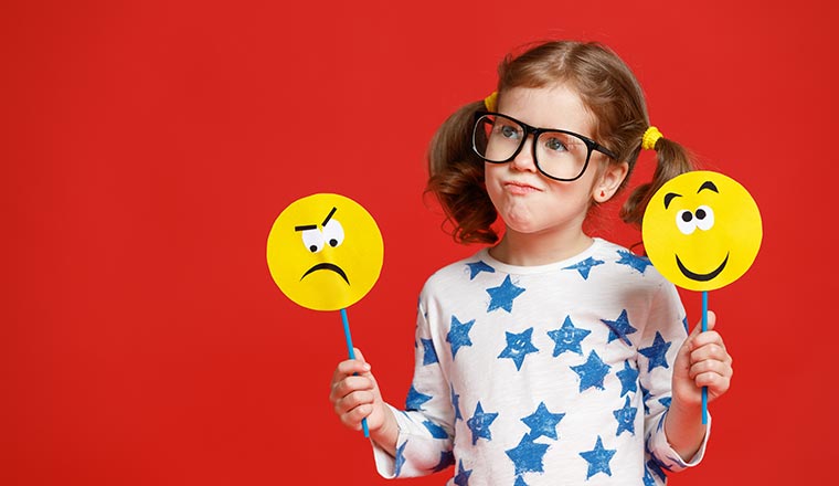 A girl holds to emoji faces- one is angry and the other is smiley