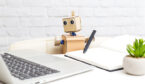 A photo of a cardboard robot holding a pen and looking at a laptop