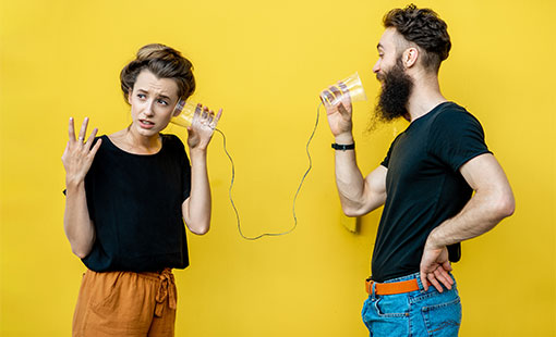 A photo of two people talking and listening through cups