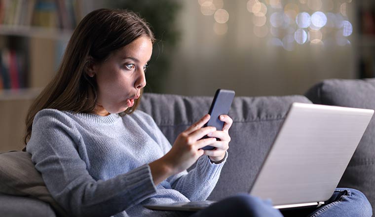 A person looking at a mobile phone with a laptop on her lap