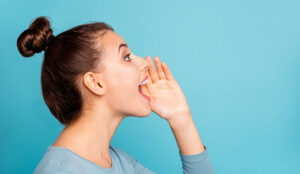 A lady hold her hand up to her mouth while yelling. There is a light blue background