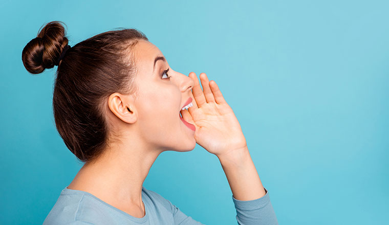 A lady hold her hand up to her mouth while yelling. There is a light blue background