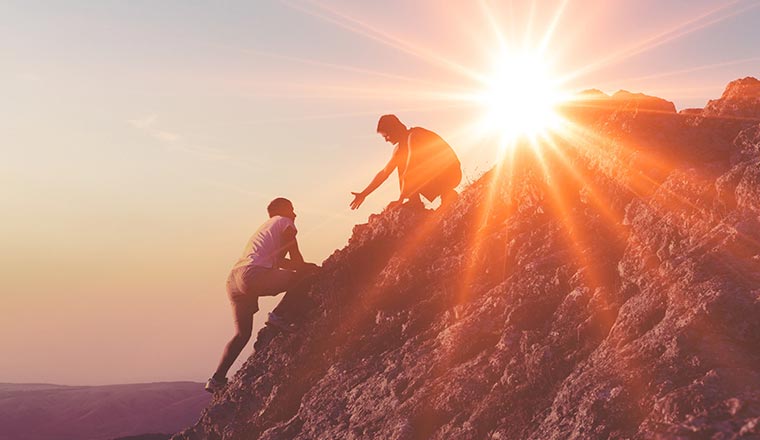 A photo of someone helping another person up a cliff