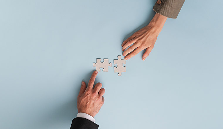 A photo of two busiess hands connecting puzzle pieces