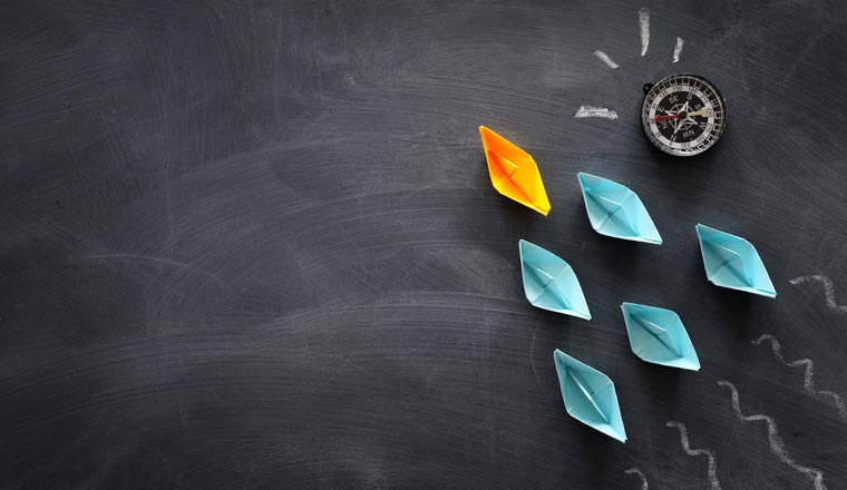 A picture of paper boats with a leader on a blackboard