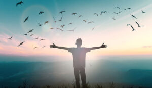 A picture of someone with their arms open and birds flying