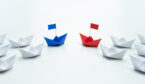A picture of blue and red paper ship leading a team of white ships
