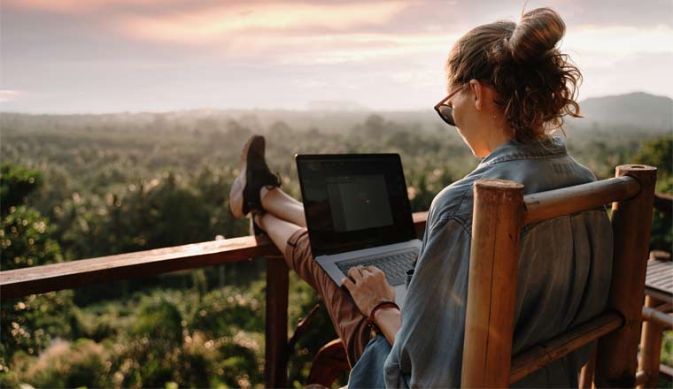 A picture of a woman working on a laptop overlooking nature