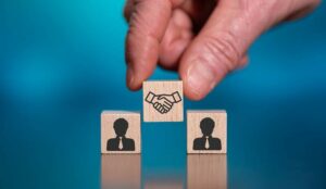 A picture of a hand placing a wooden block showing a handshake inbetween two blocks with people on them