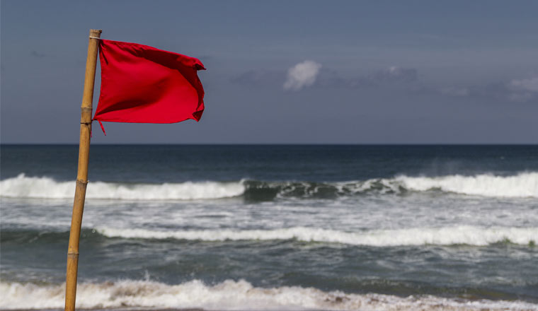 Red warning flag flapping in the wind on beach at stormy weather.