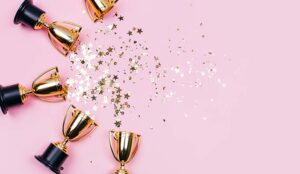 Golden winner cups with sparkles on a pink background