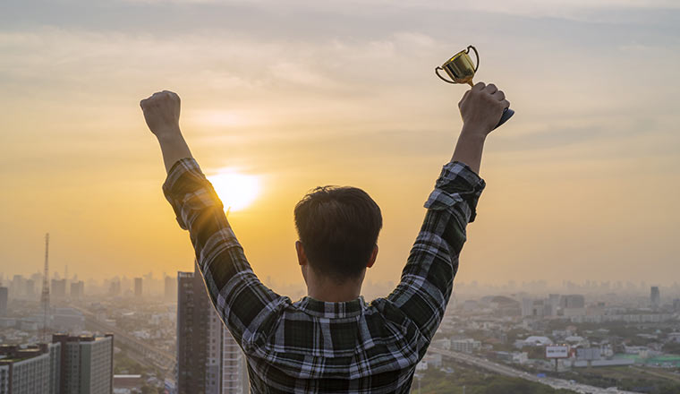 Person standing on a tall building, holding a gold trophy