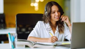 A person on a headset sat in front of a laptop making notes