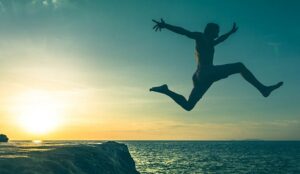 Person jumping over a cliff into the sea on sunset