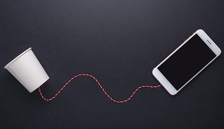 Two white paper cup connect with red rope used for classic phone and modern smartphone on black stone table board.