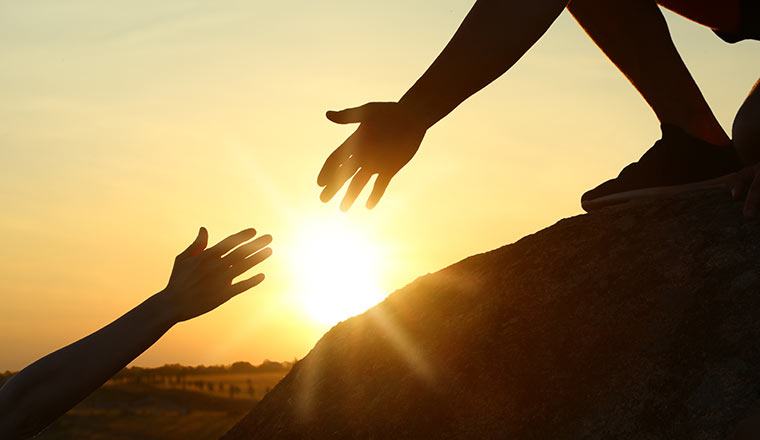 Person helping friend outdoors at sunset