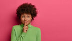 Person with finger on lips on a pink background