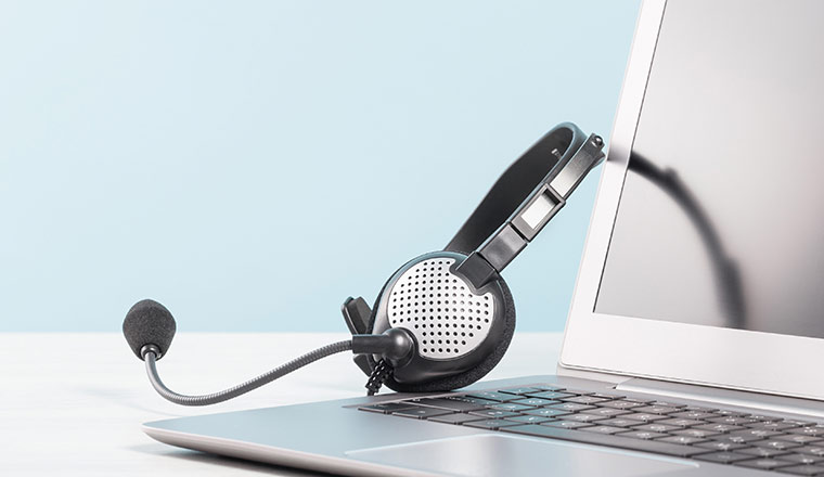 Part of Laptop with blank screen with headphones on desk blue background.