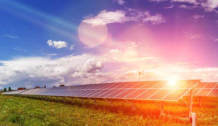 Panels of the solar energy plant under the blue sky with white clouds with sun flare hitting the surface