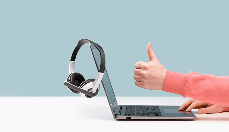 Side view of slim laptop and like thumb up hand. wireless headphones on grey desk.