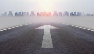 A picture of a road heading into a city with a white arrow on the tarmac