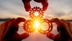 Hands holding cogs with a sunset in the background