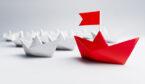 White paper boats with a red boat with a flag leading