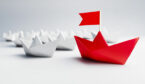 White paper boats with a red boat with a flag leading