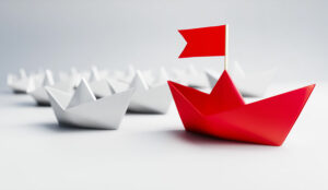 White paper boats with a red boat with a flag leading