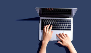 Person using a laptop computer from above on a blue background