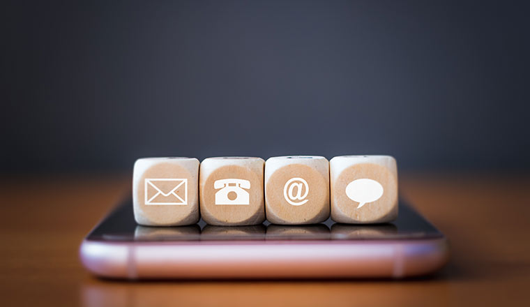 Close-up of a phone, email, chat and post icons wooden dice arranging in a row on mobile phone