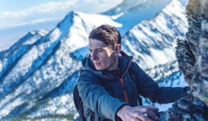 Hiking with a backpack crawling on rocky rocks to the top on the background of snowy mountains