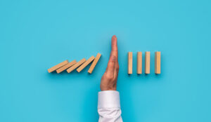 A hand stopping falling dominos on blue background