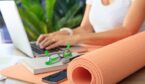 Person on a laptop in the background with exercise mat in foregraound