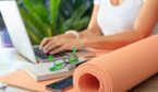 Person on a laptop in the background with exercise mat in foregraound