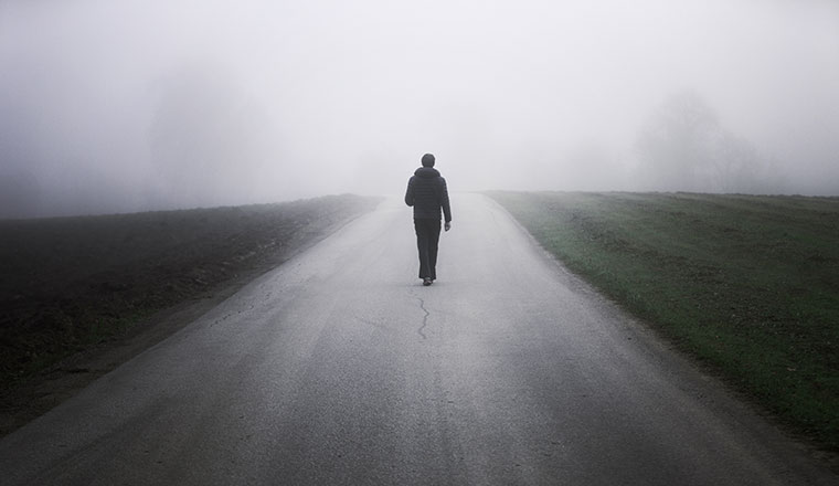 Person walking alone on rural misty asphalt road