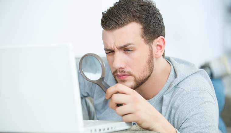 Person concentrated looking through a magnifying glass on laptop