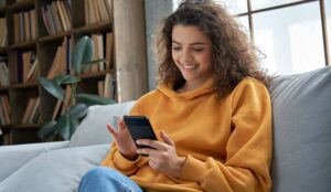 A happy person sat on a sofa checking their phone