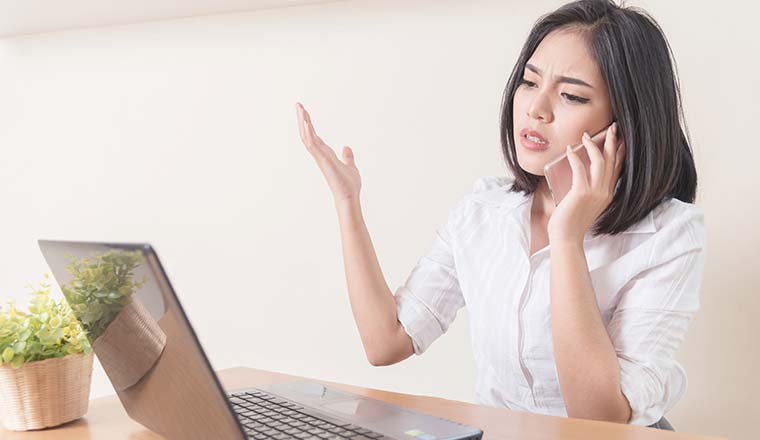 Frustrated person on phone in front of laptop