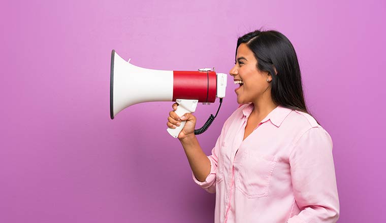 Person in front of purple wall shouting through a megaphone