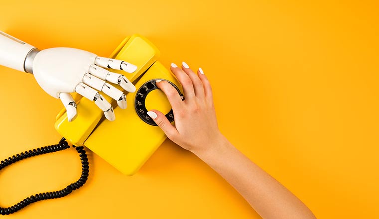 A human hand and robot hand reaching for vintage phone on yellow background