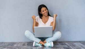 Person celebrating while sitting with laptop computer isolated over gray background.