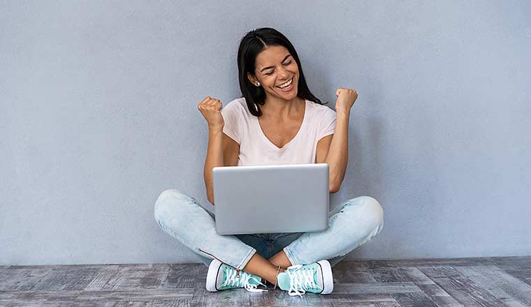 Person celebrating while sitting with laptop computer isolated over gray background.