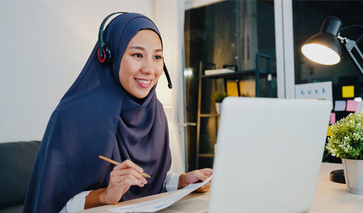 A person wearing a headset sat in front of a laptop making notes