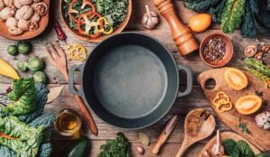 Various ingredients and empty iron cooking pot, wooden bowls, spoons on wooden background.