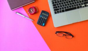 Top view of laptop and office supplies on colourful background.