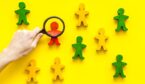 Wooden figures of people under black magnifying glass on yellow background