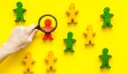 Wooden figures of people under black magnifying glass on yellow background