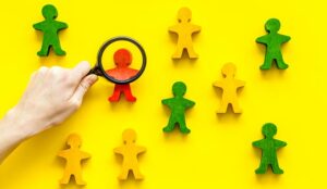 Wooden figures of people under black magnifying glass on yellow background